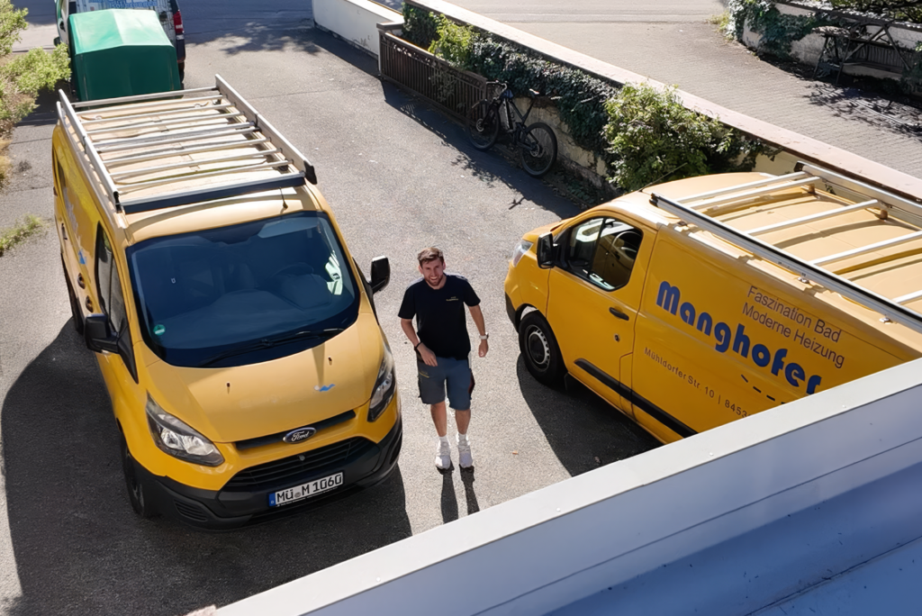 Christoph Manghofer zwischen zwei Manghofer-Servicefahrzeugen vor einem Kundeneinsatz.
